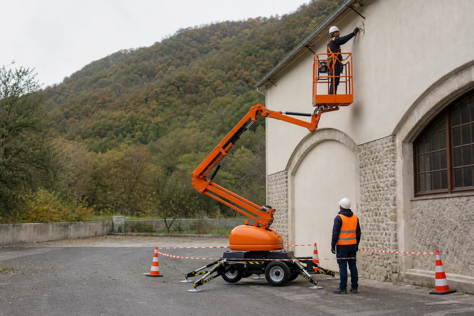 Une nacelle élévatrice orange intervient sur un bâtiment avec un technicien dans le panier et un opérateur au sol, dans le secteur de Privas.