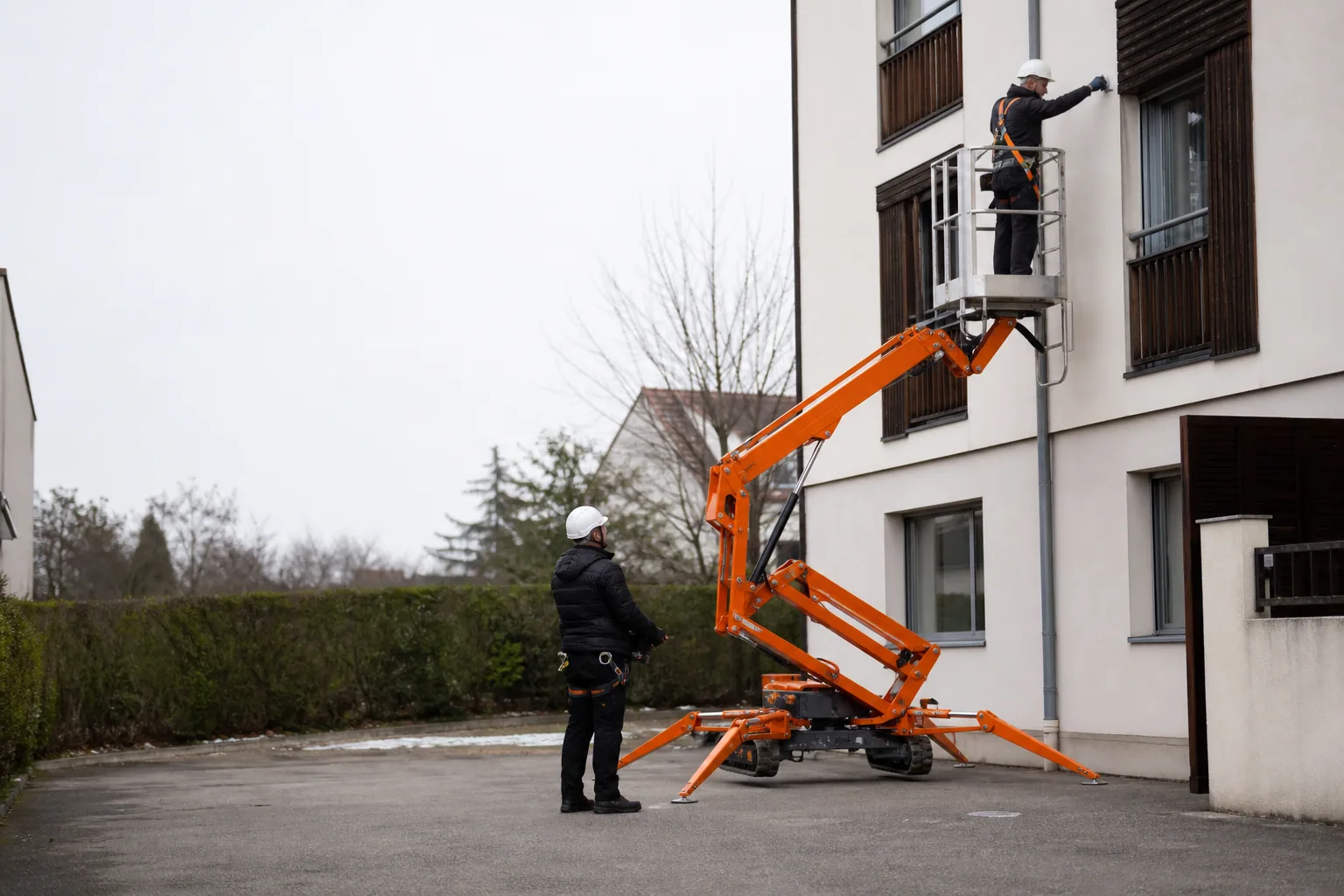 Une nacelle élévatrice orange intervient sur un bâtiment avec un technicien dans le panier et un opérateur au sol, dans le secteur de Strasbourg.